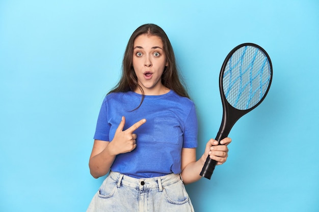 Vrouw met een elektrische bug zapper op een blauwe achtergrond die naar de zijkant wijst