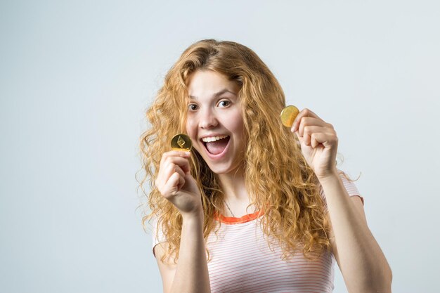Vrouw met een fysieke bitcoin in haar hand op een grijze achtergrond Emotioneel portret van een meisje met cryptocurrency