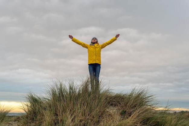 Vrouw met een gele jas op de top van een zandduin met haar armen omhoog succesconcept