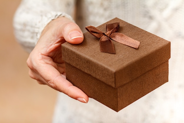 Vrouw met een geschenkdoos in haar hand. Ondiepe scherptediepte, selectieve focus op de doos. Concept van het geven van een cadeau op vakantie of verjaardag.