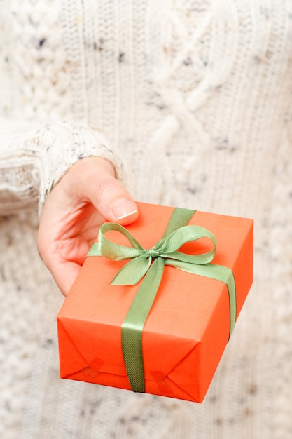 Vrouw met een geschenkdoos vastgebonden met een groen lint in haar hand. Ondiepe scherptediepte, selectieve focus op de doos. Concept van het geven van een cadeau op vakantie of verjaardag.