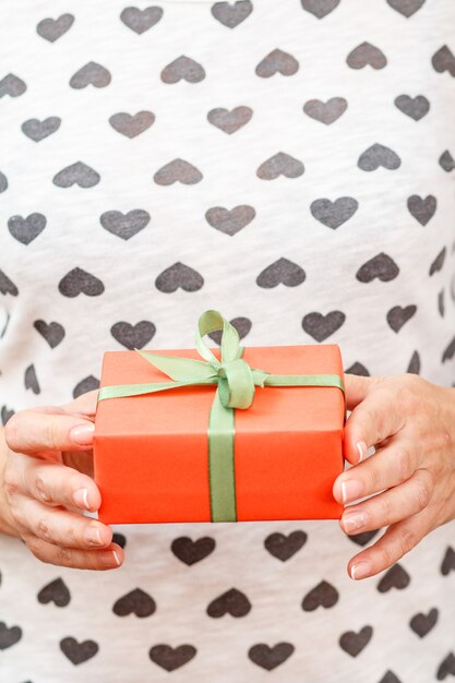 Vrouw met een geschenkdoos vastgebonden met een groen lint in haar handen. Ondiepe scherptediepte, selectieve focus op de doos. Concept van het geven van een cadeau op vakantie of verjaardag.