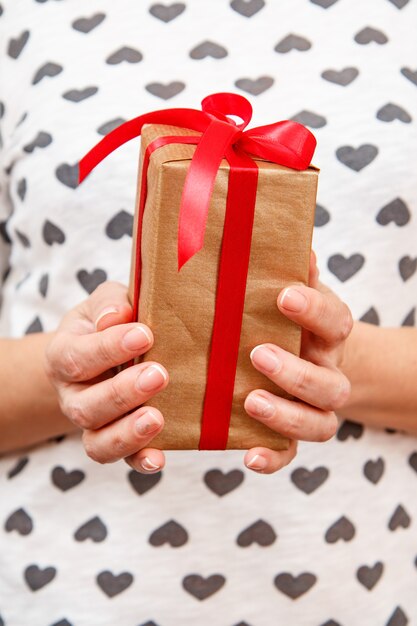 Vrouw met een geschenkdoos vastgebonden met een rood lint in haar handen. ondiepe scherptediepte, selectieve focus op de doos. concept van het geven van een cadeau op vakantie of verjaardag.