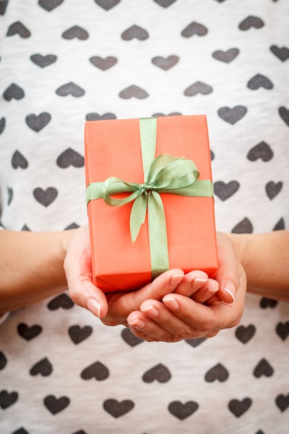 Vrouw met een geschenkdoos vastgebonden met een rood lint in haar handen. Ondiepe scherptediepte, selectieve focus op de doos. Concept van het geven van een cadeau op Valentijnsdag of verjaardag.