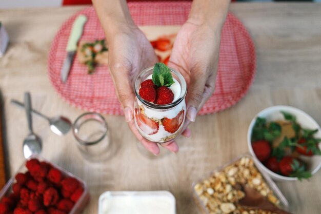 Foto vrouw met een glas aardbeienparfait met yoghurt en granola