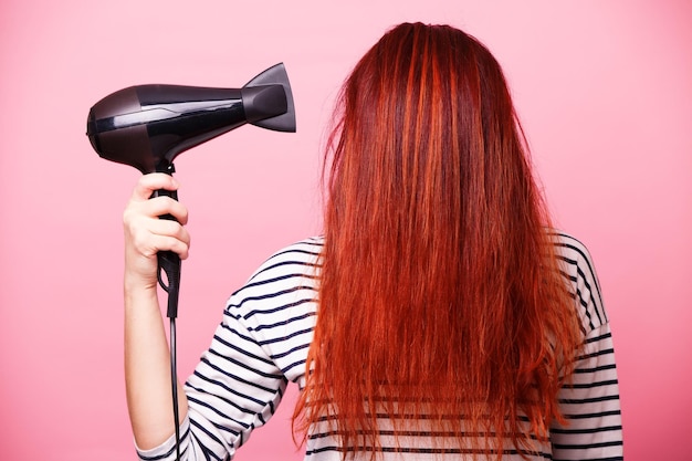 Vrouw met een haardroger op een roze achtergrond