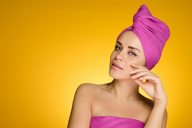 Vrouw met een handdoek op haar hoofd na een douche poseert op de camera op een gele achtergrond