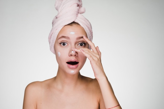 Vrouw met een handdoek op haar hoofd smeert crème op haar gezicht