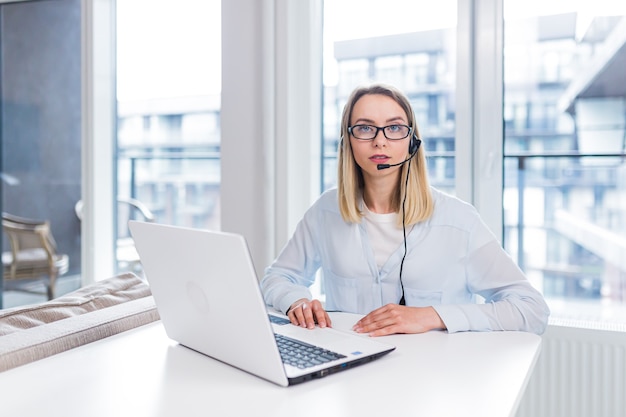 vrouw met een headset en bril communiceert met klanten op afstand van een laptop