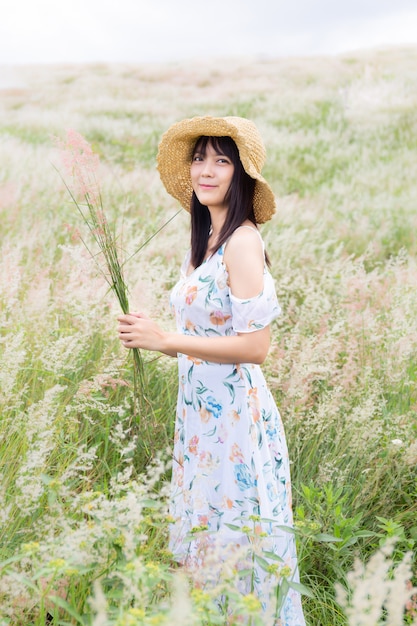 vrouw met een hoed, gekleed in een witte jurk, staande in het midden van het gras met prachtige witte bloemen met een ontspannen en vrolijke sfeer.