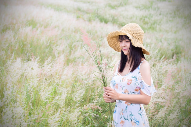 vrouw met een hoed, gekleed in een witte jurk, staande in het midden van het gras met prachtige witte bloemen met een ontspannen en vrolijke sfeer.