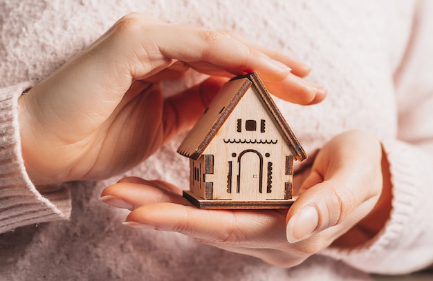 Vrouw met een houten huis met haar handen met de zon op een lichtroze ruimte