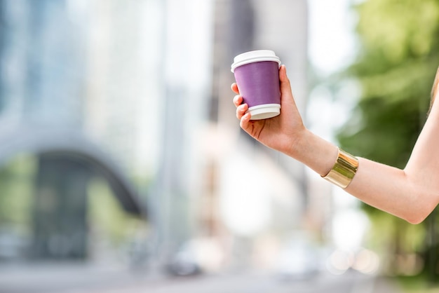 Vrouw met een koffiekopje om mee te nemen met kopieerruimte buiten op de achtergrond van de moderne stad