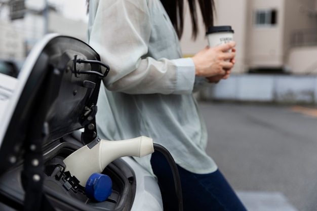 Vrouw met een koffiepauze terwijl haar elektrische auto wordt opgeladen