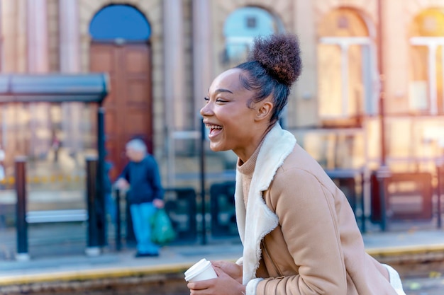 vrouw met een kopje koffie Een lachende krullend brunette dame in een trui te wachten op een tram