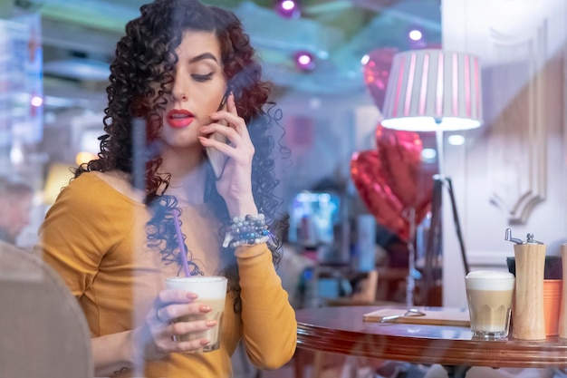 Vrouw met een kopje koffie spreekt aan de telefoon terwijl ze aan een tafel in een café zit