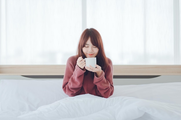 Vrouw met een kopje koffie thee melk op het bed in een witte kamer Vrouw drinkt