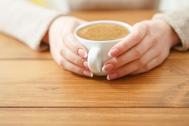 Vrouw met een kopje koffie zittend aan houten tafel, ondiepe scherptediepte.