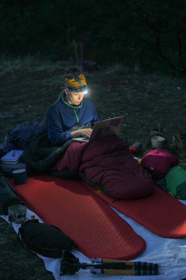 Foto vrouw met een laptop terwijl ze in de schemering op het veld kampeert