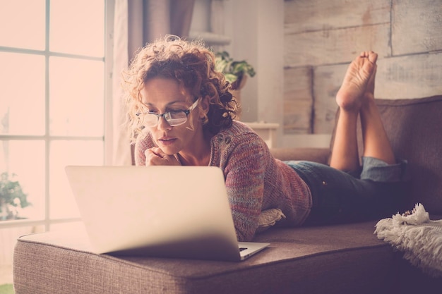 Foto vrouw met een laptop terwijl ze thuis op de bank ligt