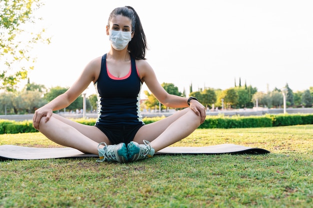 Vrouw met een masker die de lotus yoga positie in een openbaar park