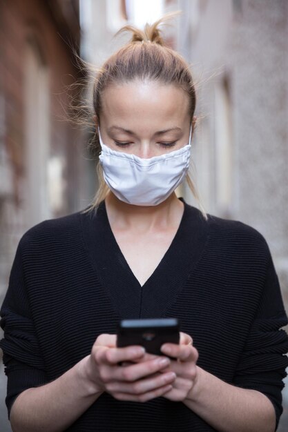 Foto vrouw met een masker die een smartphone gebruikt en buiten staat