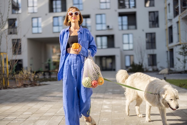 Vrouw met een meshbag met verse boodschappen terwijl ze met haar hond naar huis loopt