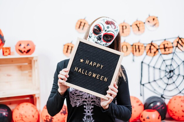 Foto vrouw met een mexicaans gezichtsmasker tijdens halloweenvrouw met een briefbord met een skeletkostuum