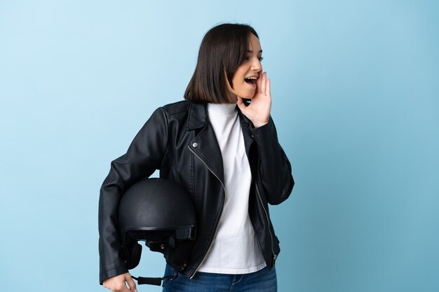 Vrouw met een motorhelm geïsoleerd op blauw schreeuwen met mond wijd open aan de zijkant