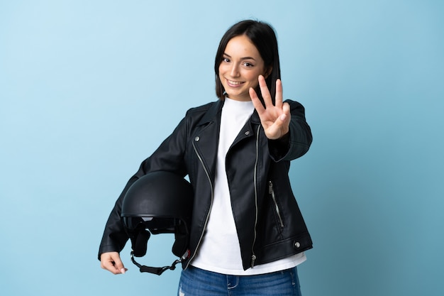 Vrouw met een motorhelm geïsoleerd op blauwe achtergrond gelukkig en drie tellen met vingers