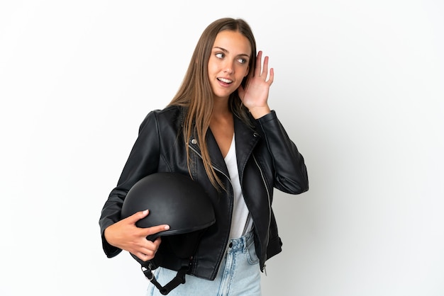 Vrouw met een motorhelm over een geïsoleerde witte achtergrond die naar iets luistert door de hand op het oor te leggen