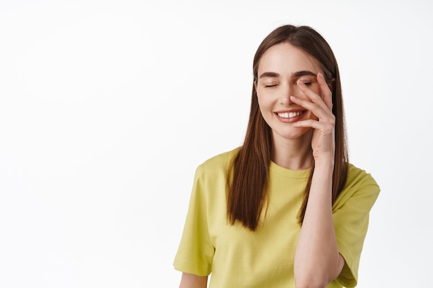 Vrouw met een natuurlijke, frisse schone huid, blozend en kegelvormig gezicht met de hand, gelukkig lachend, staande op wit