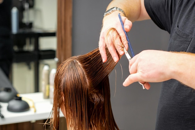 Vrouw met een nieuw kapsel. Mannelijke herenkapper die bruin haar knippen met een schaar in een kapsalon.