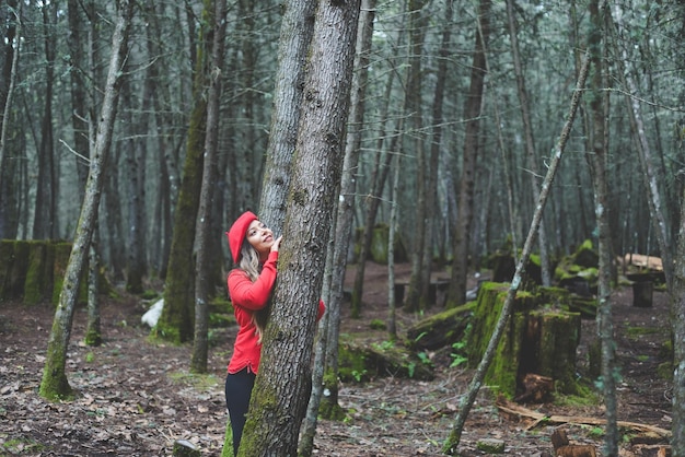 Vrouw met een peinzende houding die het bos bewondert, leunend tegen een boomstam