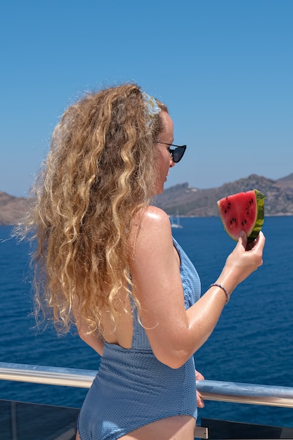 Vrouw met een plakje watermeloen in een strooien hoed in de buurt van de zee