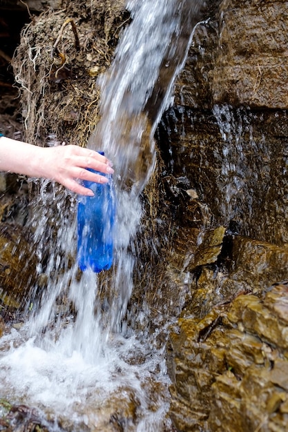 Vrouw met een plastic fles die schoon water uit de koude bron haalt