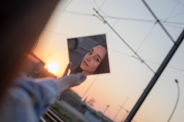 Vrouw met een spiegel tegen de hemel bij zonsondergang