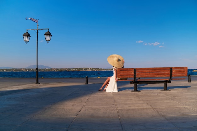 Vrouw met een strohoed die op een houten bank zit in de spetses-jachthaven, griekenland