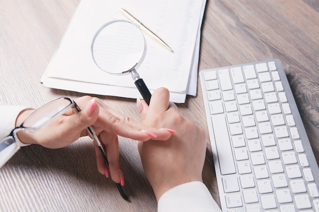 Vrouw met een vergrootglas kijkt naar papier op het bureaublad