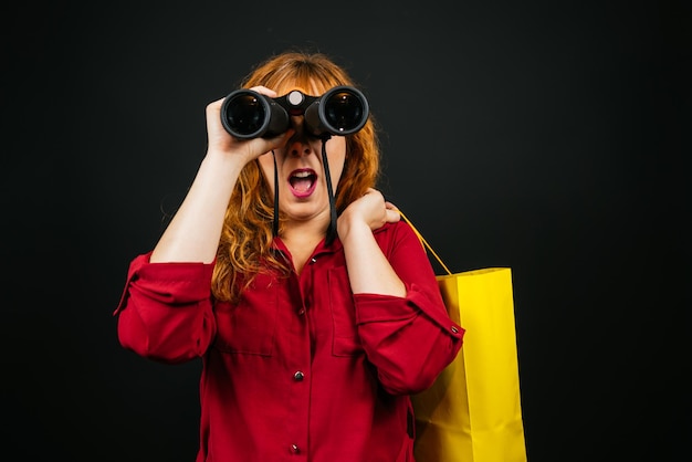 Vrouw met een verrekijker en een boodschappentas die naar de camera kijkt op een zwarte achtergrond met mist