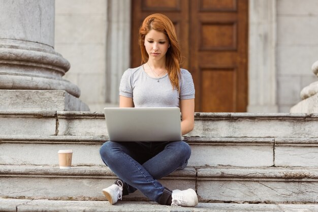 Vrouw met een wegwerpbeker met behulp van laptop