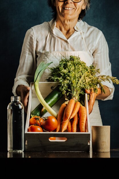 Foto vrouw met een witte doos met groenten boven een tafel met water in de buurt van haar, gezonde voeding concept met kopie ruimte