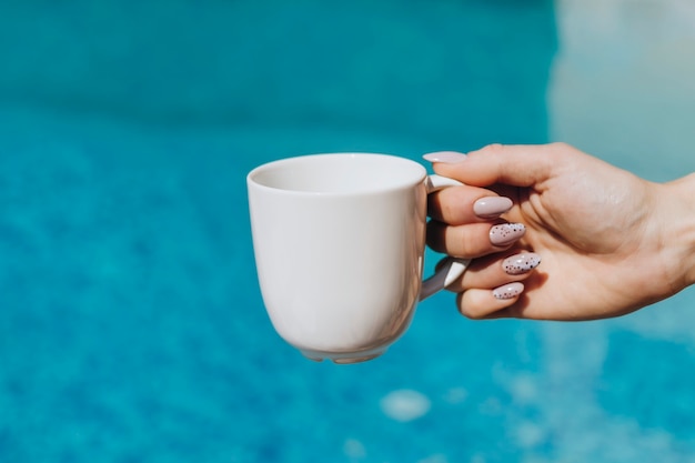 Vrouw met een witte koffiekop bij het zwembad