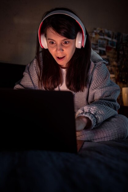 Vrouw met een wonder gezicht zittend op het bed kijkend naar een hoofdtelefoon met een laptopscherm