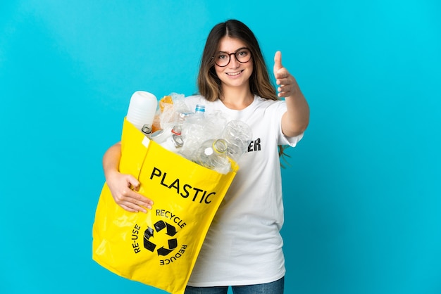 Vrouw met een zak vol flessen om te recyclen geïsoleerd op blauwe muur handen schudden voor het sluiten van een goede deal