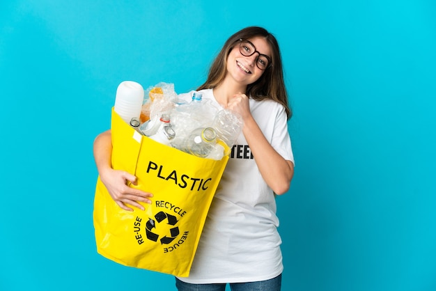 Vrouw met een zak vol flessen om te recyclen op blauw en viert een overwinning