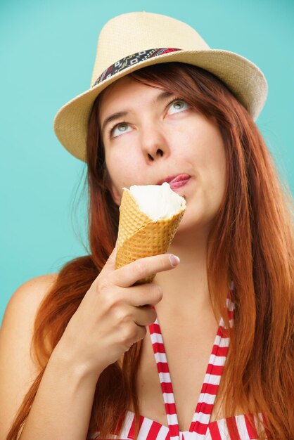 Vrouw met een zwempak en een strohoed eet een ijsje uit de beker op een kleurrijke turquoise achtergrond