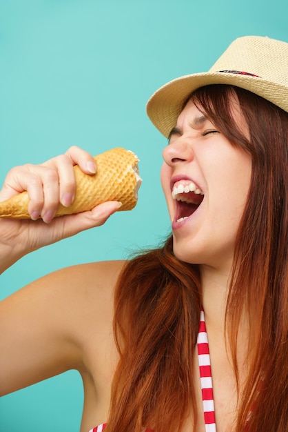 Vrouw met een zwempak en een strohoed eet een ijsje uit de beker op een kleurrijke turquoise achtergrond