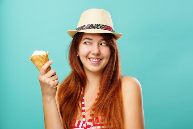 Vrouw met een zwempak en een strohoed eet een ijsje uit de beker op een kleurrijke turquoise achtergrond