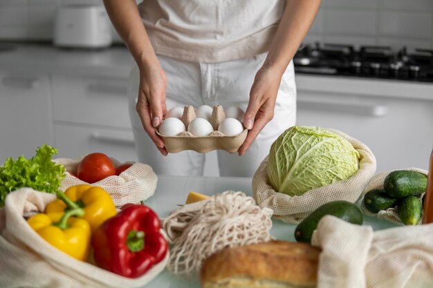 Foto vrouw met eierbakje met herbruikbare boodschappentassen met groenten op een tafel in een keuken